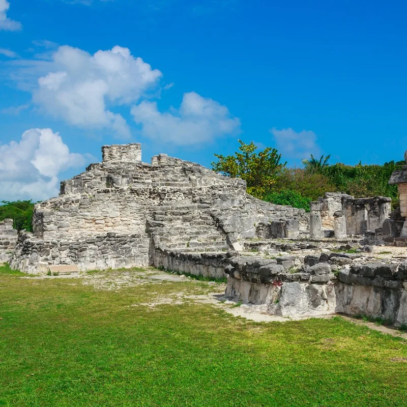 El Rey Mayan site near Cancun, blue skies and clouds, grassy area around the ruins. 
