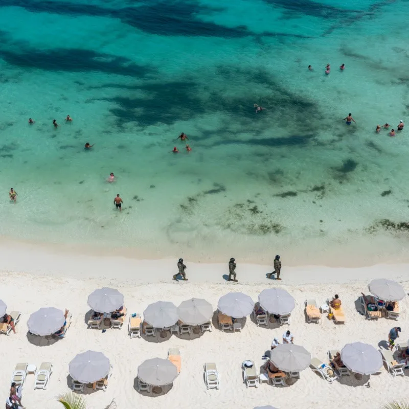 Military Walking on a Cancun Beach while tourists sunbathe and swim in the sea.