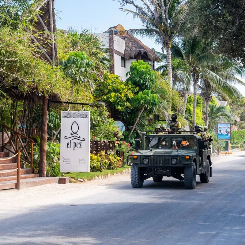 Military on Tulum Street driving down the road in front of a restaurant.