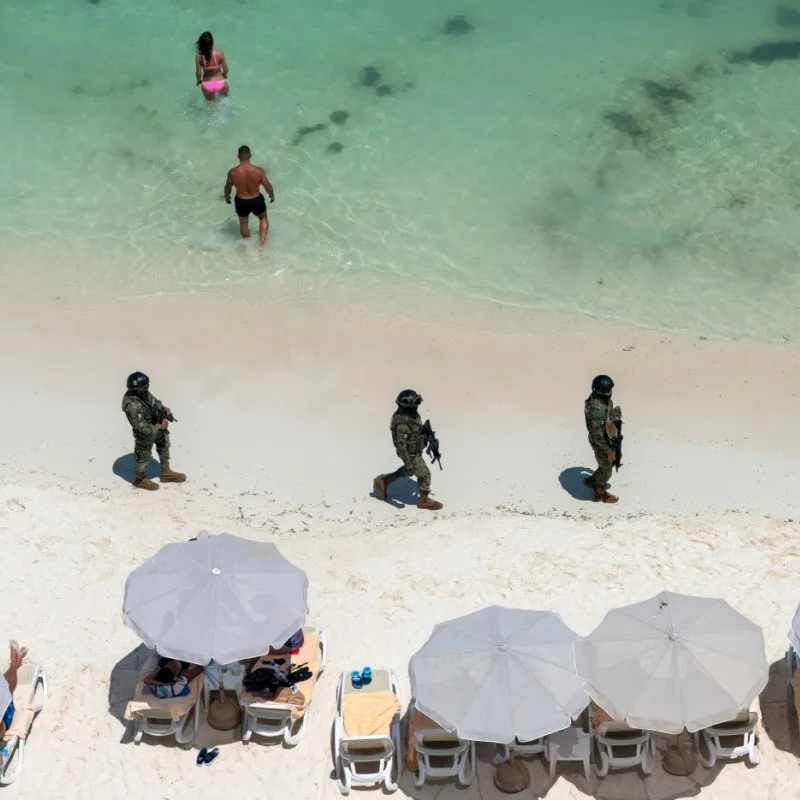 Military on the Beach in Cancun with tourists in the background and beach chairs with umbrellas.
