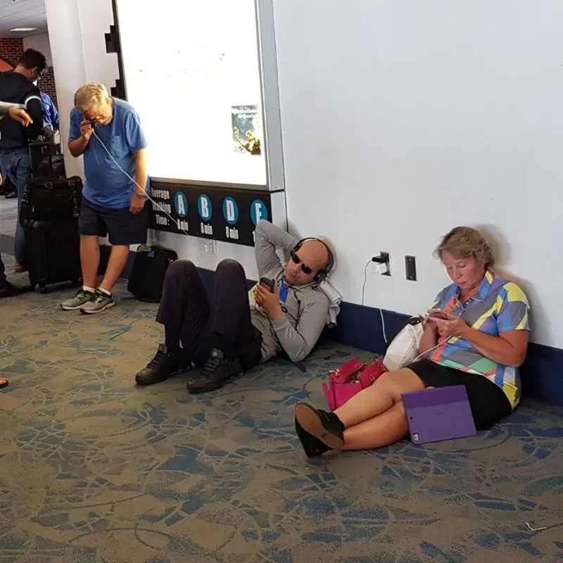 Passengers sitting in the floor and charging their phones in the corridors of the airport due flight delays