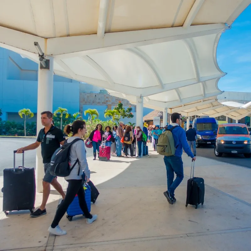 People Standing Outside of Cancun Airport with their luggage and busses and veicles nearby.