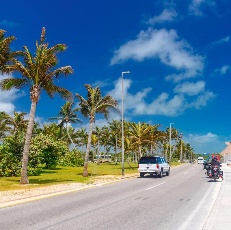 SUV driving on the road with palms on a sunny day near Cancun, Mexico.