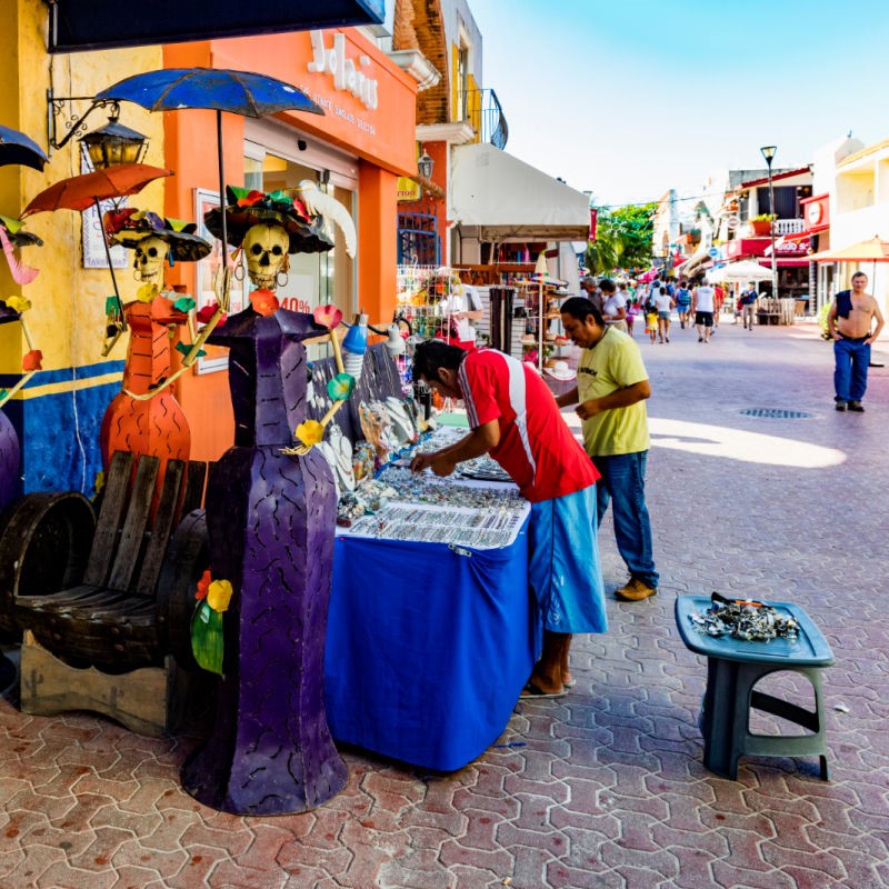 Shops on 5th Avenue in Playa del Carmen with people walking down the street.