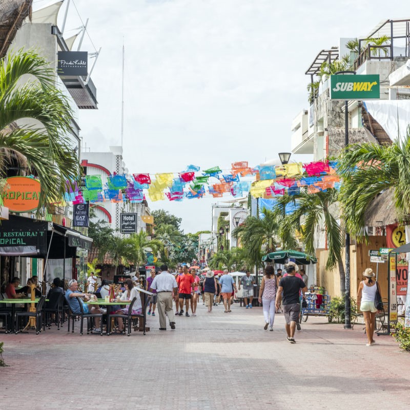 5th Avenue Playa del Carmen, with people walking up and down the street past restaurants and shops.