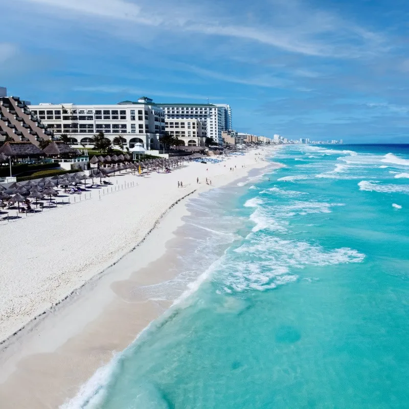 Cancun Coastline with resorts in the background and tourists on the beach.