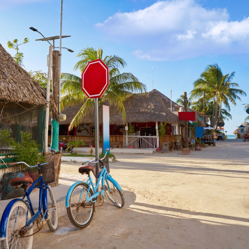 Charming Street in Holbox with two bikes in front of a house with the beach in the distance.