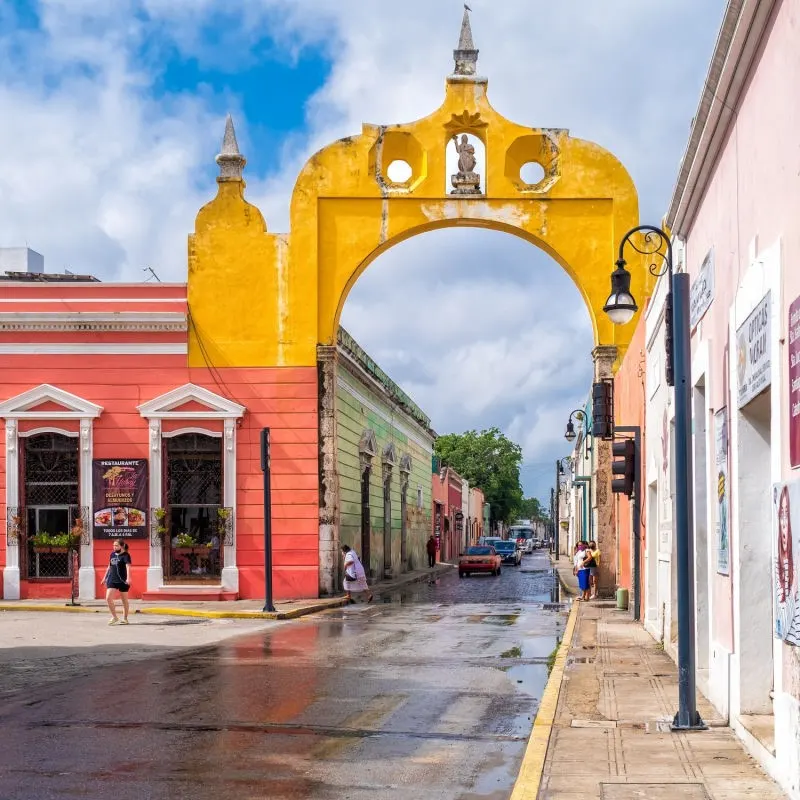 Street in Merida with colorful colonial buildings and people walking around.