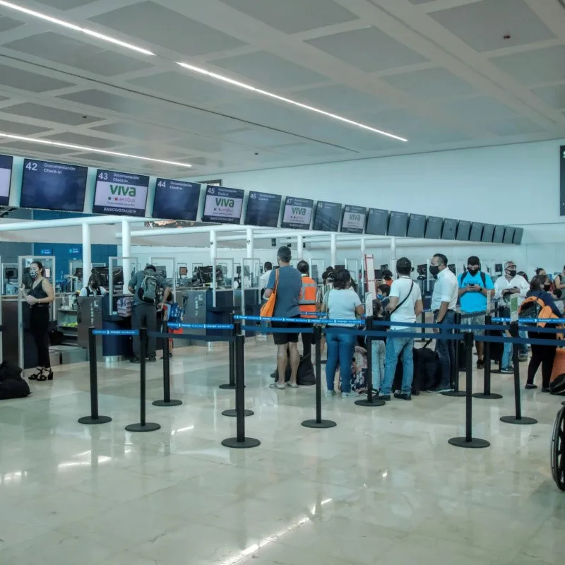 Tourists Checking in at Cancun Airport, waiting in line and talking on the phone.