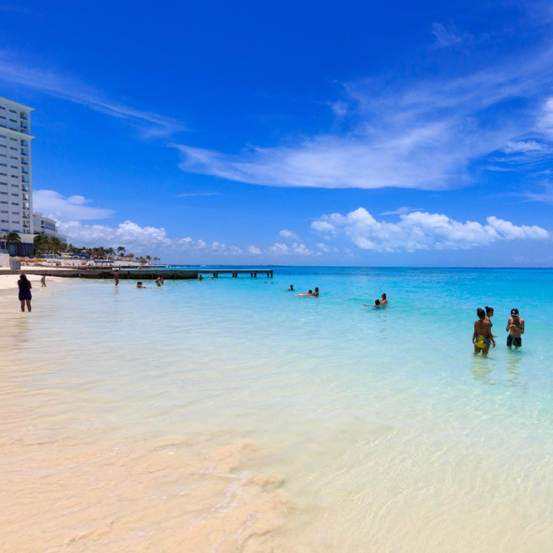 Tourists Swimming in the Cancun Hotel Zone with a resort in the background.