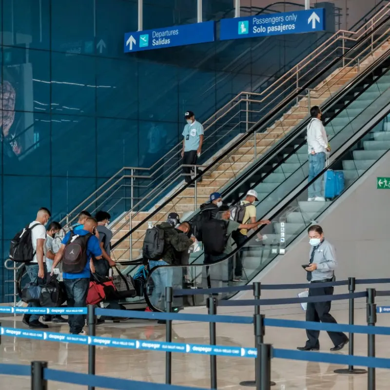 Tourists at Cancun Airport going up and down escalators with luggage.