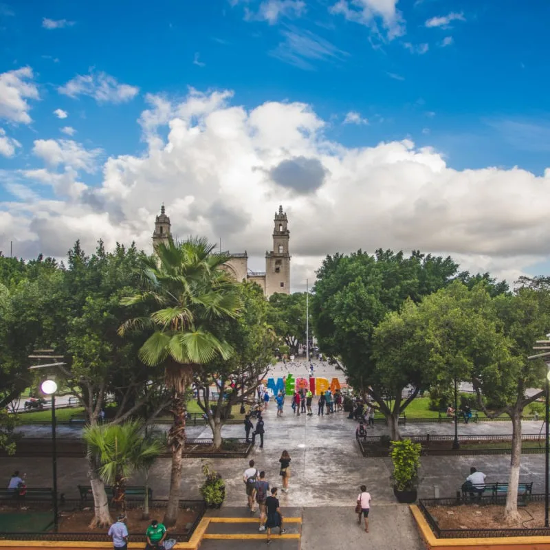 Tourists in Downtown Merida walking in a plaza in front of the Merida sign.