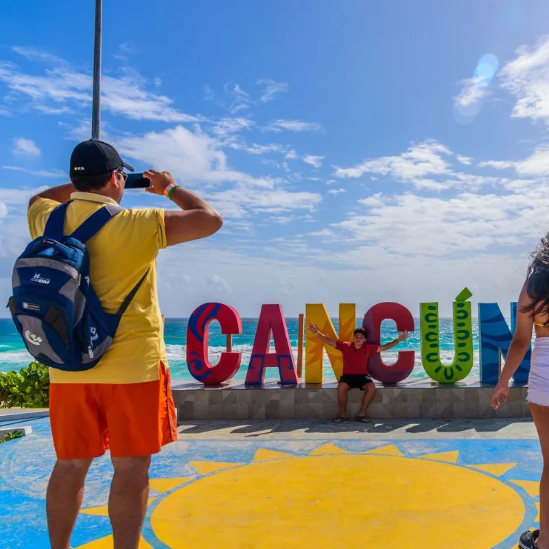 tourists standing in front of and taking pictures of the Cancun sign