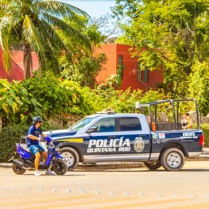 A Tulum Police Vehicle is parked on the street in front of a building with palm trees in front.