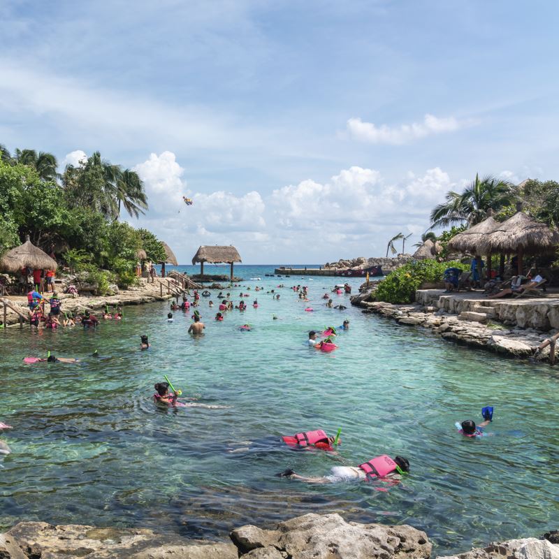 tourist and travelers Snorkeling at XCaret park on the Mayan Riviera resort on clear blue water with tiki huts on land