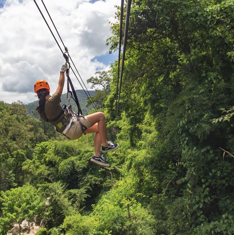 woman on vacation zip line over jungle on sunny day overlooking green trees