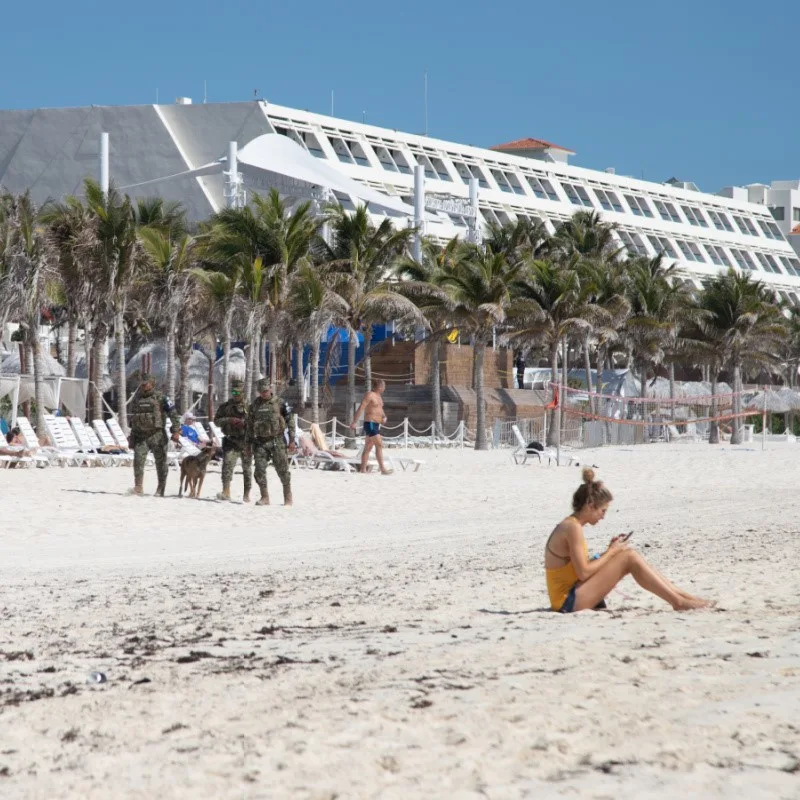 Girl Sitting on a Cancun Beach with Military Guards in the Background