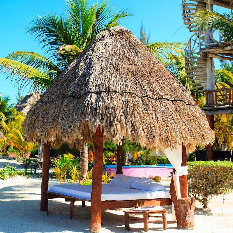 Holbox palapa beach loungers on a sunny sunny day with palm trees in the background.