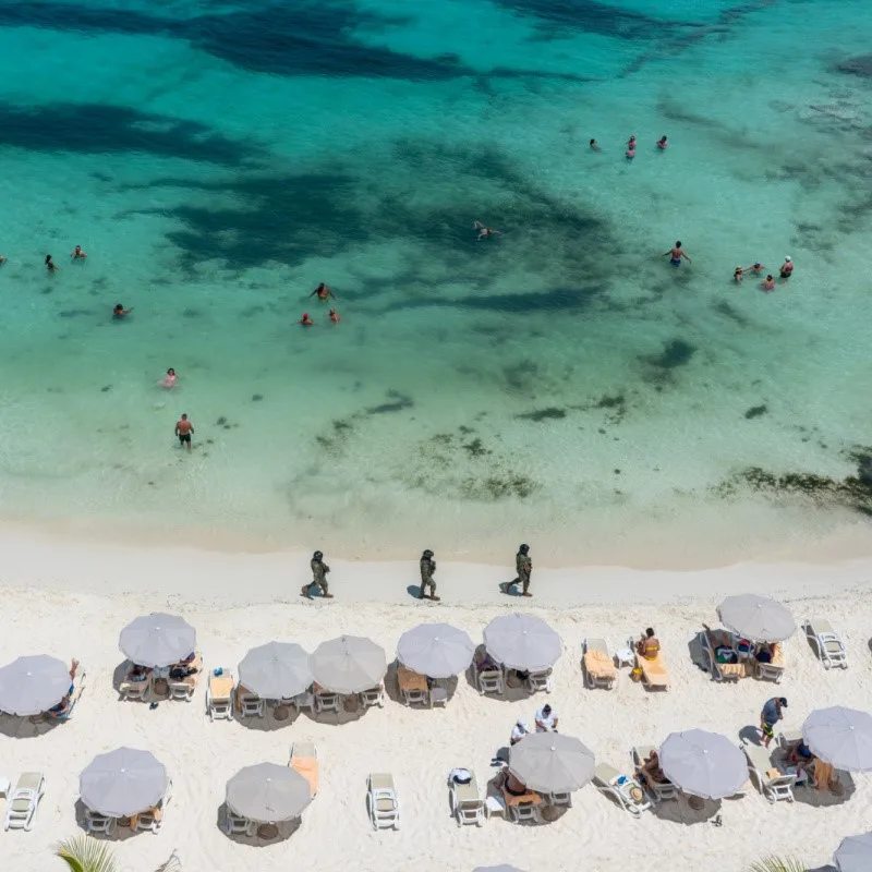 Military Walking the Beach in Cancun and Tourists in the Water