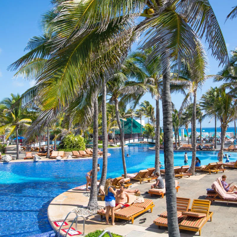 Luxurious pool area in a Cancun resort with palm trees and blue skies