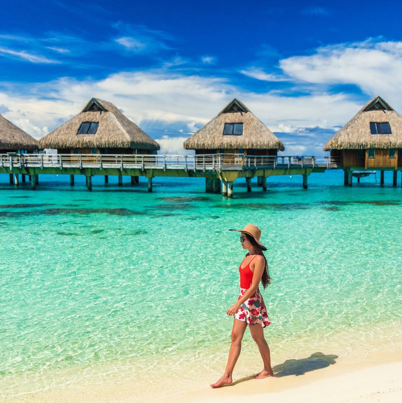 Woman walking along the beach in front of overwater bungalows