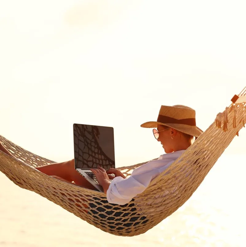 Woman working on laptop on a hammock at the beach