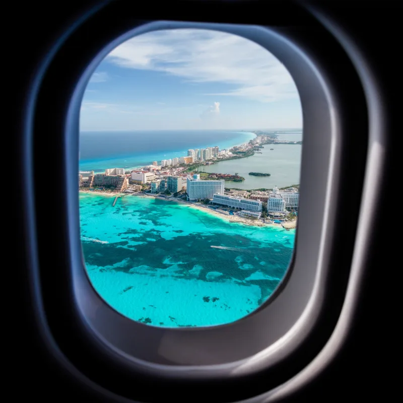 view of plane window looking out at Cancun beach during the day.