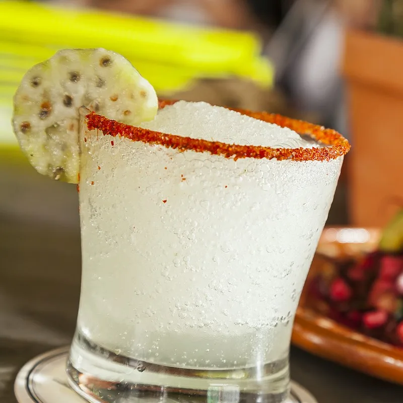 Mexican mezcal cocktail with shaved ice soda and prickly pear, out of focus hibiscus tostada on the back