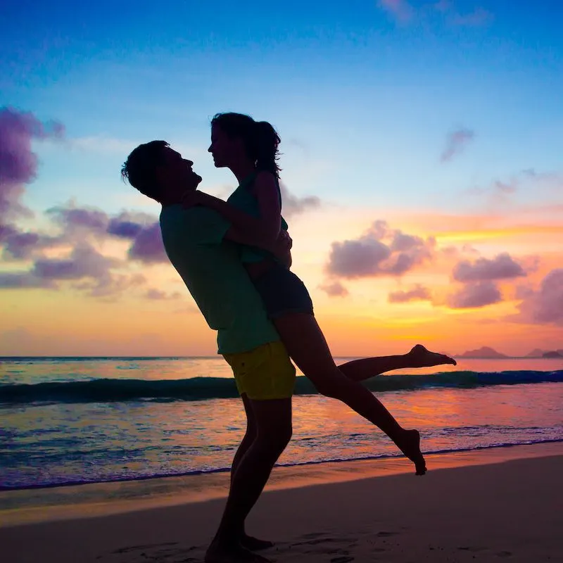 sunset silhouette of young couple in love hugging at beach.