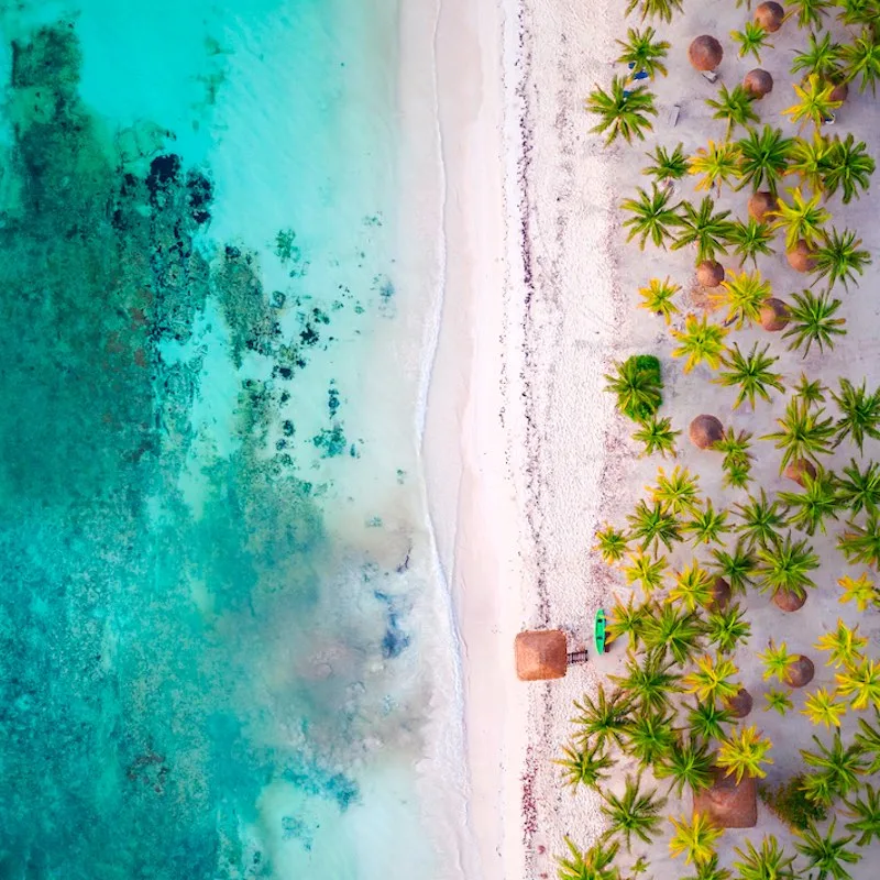 Aerial bird's eye drone view of a beautiful tropical vacation beach with crystal clear blue water, white sand, palm trees, and a kayak and lifeguard tower in Riviera Maya, Mexico near Cancun.
