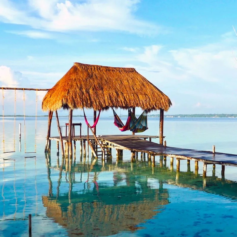 A couple on hammocks in a palapa over the water in Bacalar, Mexican Caribbean.