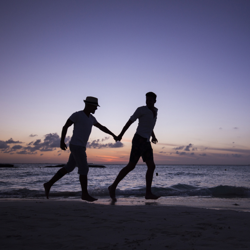 Two men running on the beach holding hands, LGBTQ+