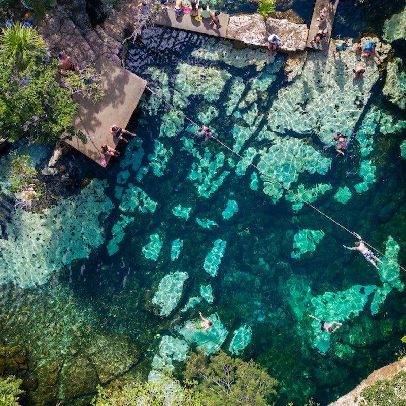 Cenote Azul in the jungle aerial view. People swim in clear water in a cenote that is in the jungle. Top view.