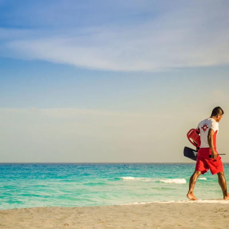 A lifeguard walking on a beach with equipment