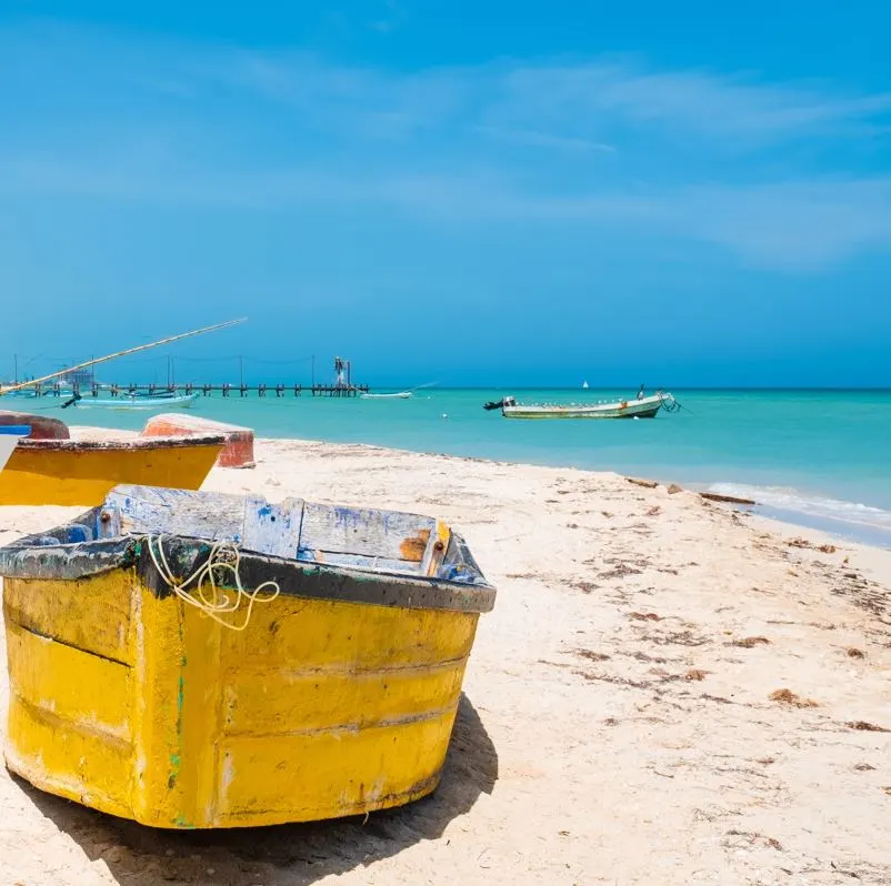 progreso beach with yellow boat on its shores, with turquoise waters in the background 