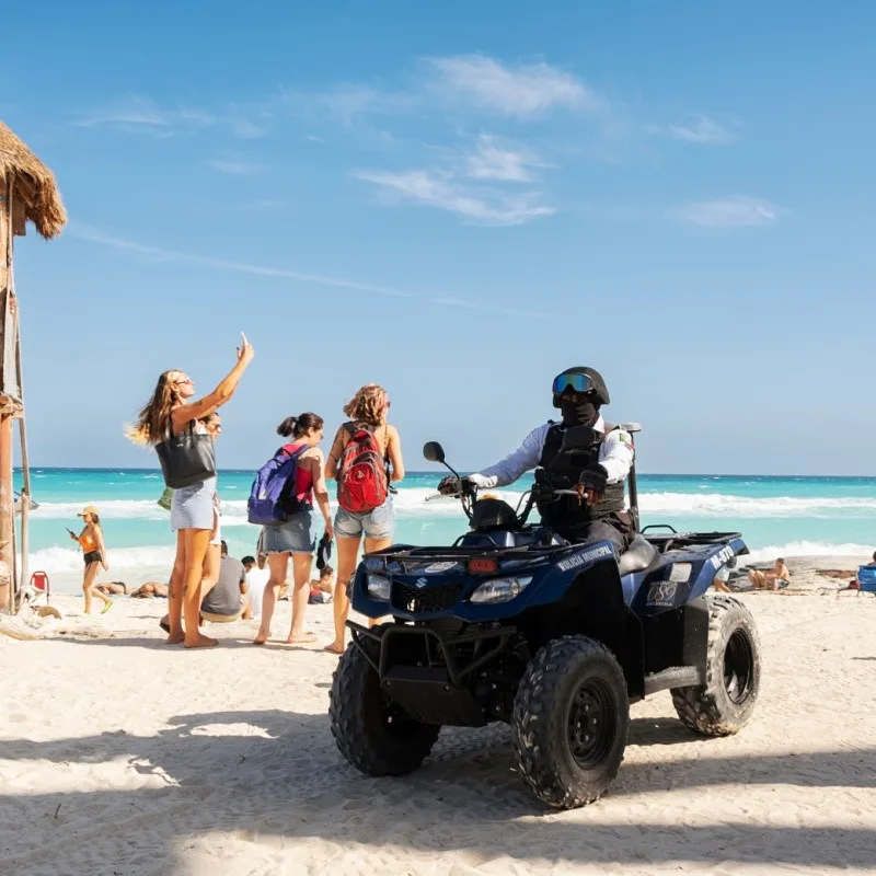 Police Officer Patrolling a Beach in Cancun, Mexico with Tourists in the Background