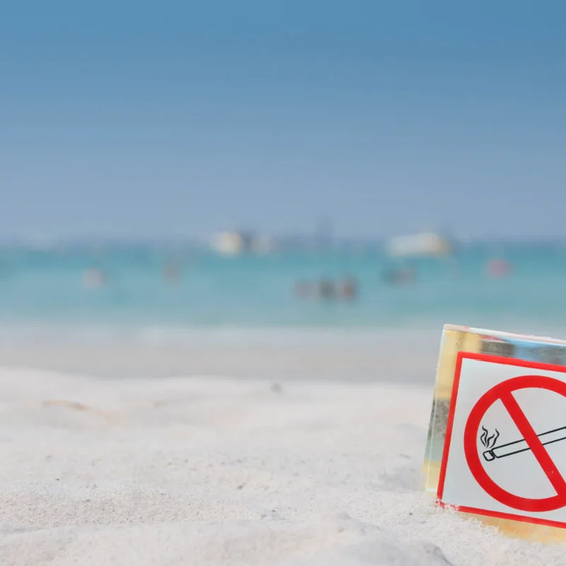 Anti-smoking sing on a beach in Cancun with water in background 