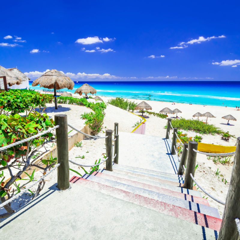 Amazing view of a beach in Cancun with entering stairs and little green trees and umbreallas