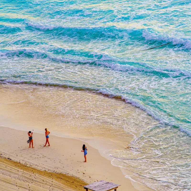 Three girls taking pictures in a Cancun Beach with the waves in the background