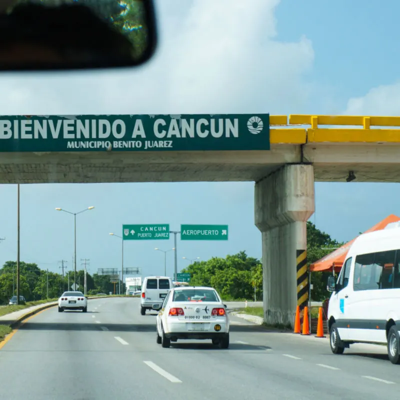 Cars and bus on the road with Welcome to Cancun sign at the front