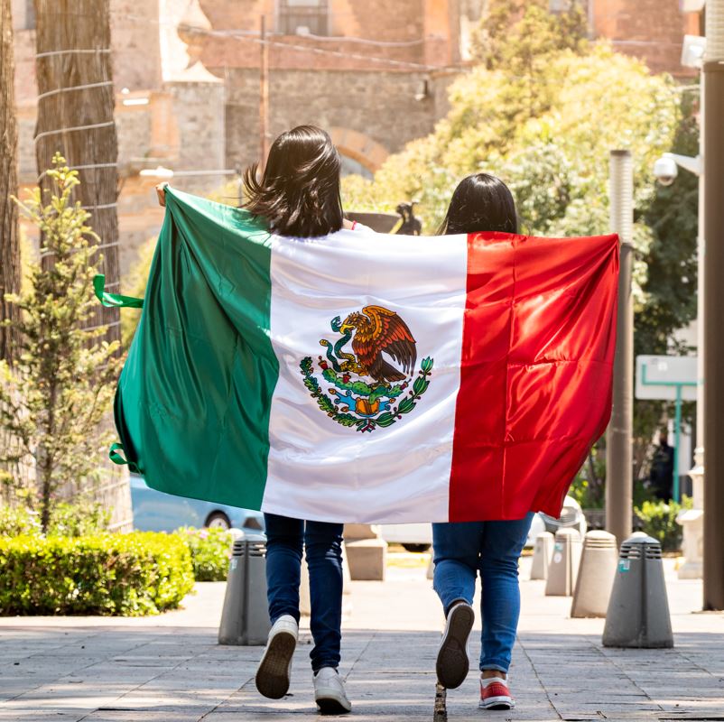 Two girls walking down a street draped in a Mexican flag