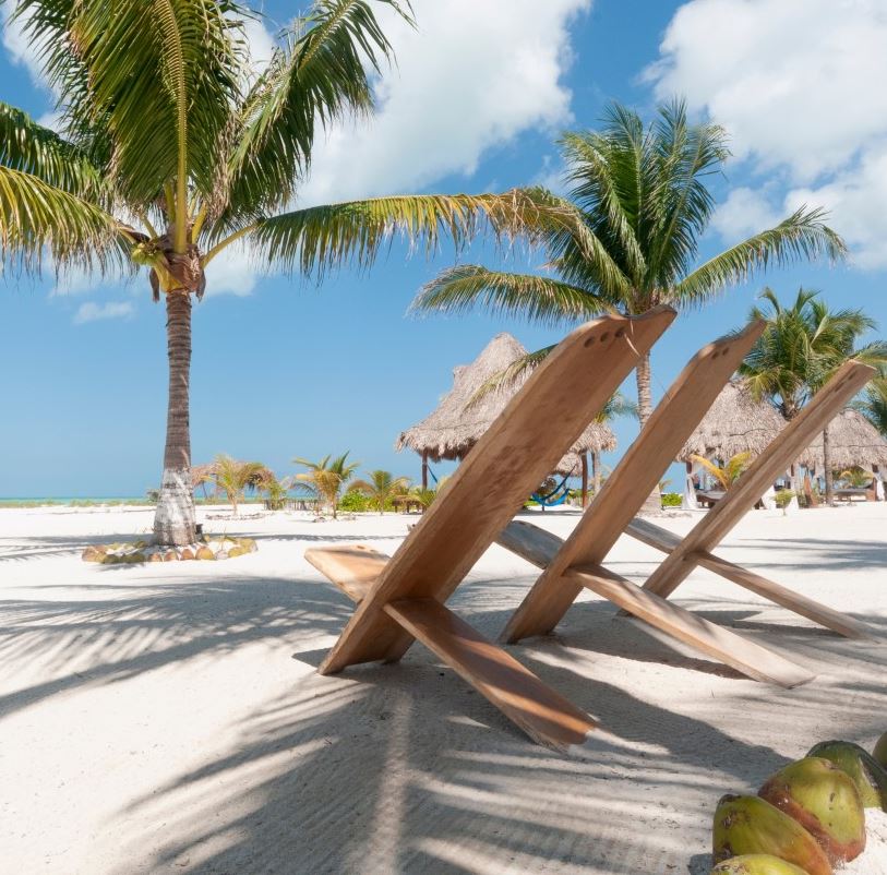 Rustic chairs on the white sand beach in the tropics with palm trees against the blue sky. Holbox Island, Mexico.
