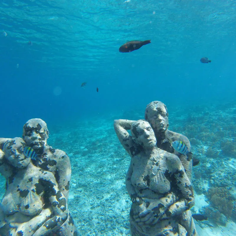 Underwater sculptures and fish in blue water in Cancun 