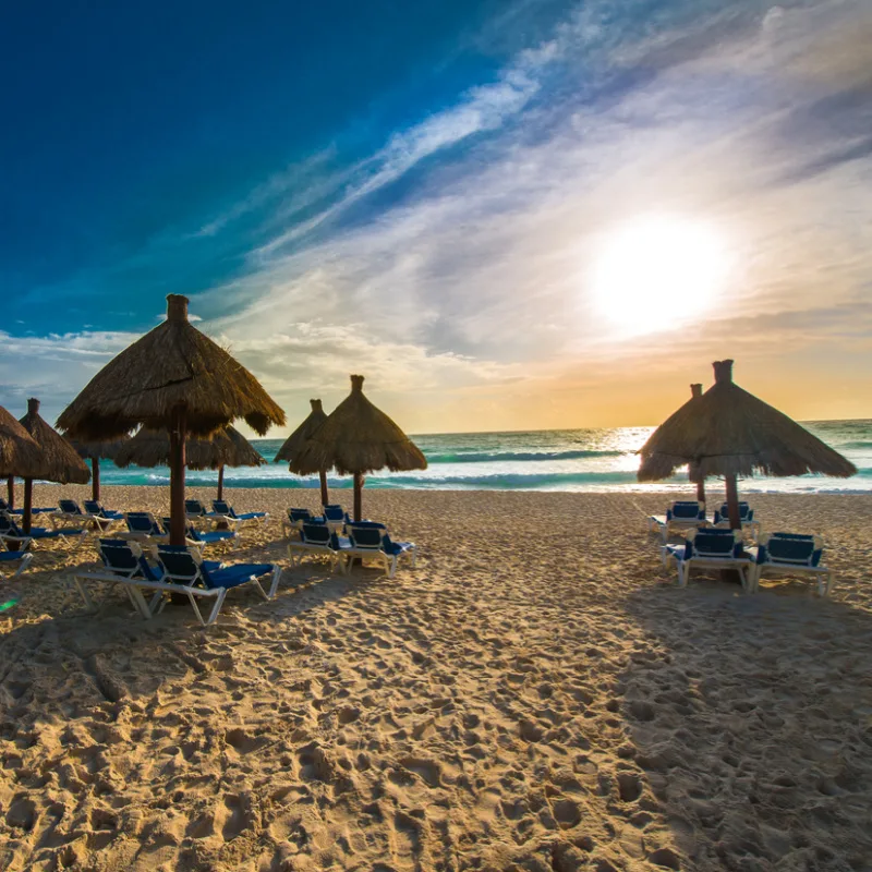 sunset in the mexican caribbean with grass umbrellas on the beach