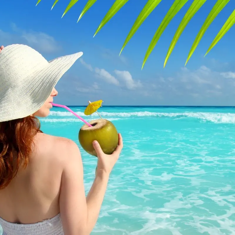 Woman drinking from coconut of Mexican Caribbean water front