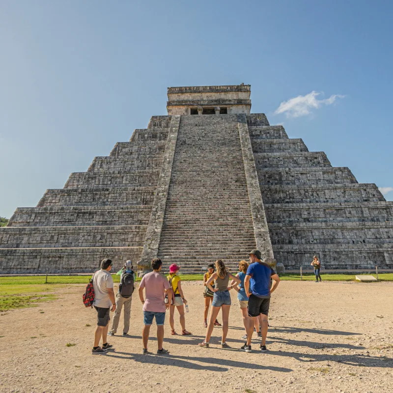 tourists at the bottom of chichen itza pyramid with tour guide
