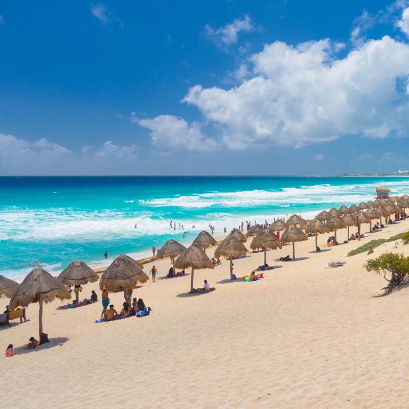 Cancun Beach with palapas and tourists on a sunny day