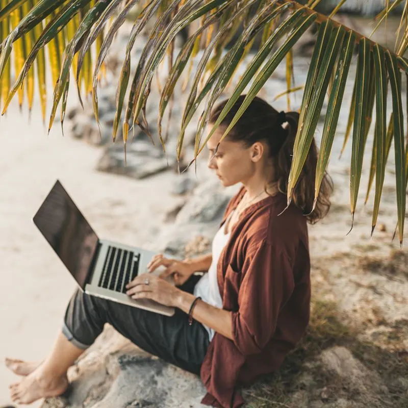 Woman with latop at the beach under a palm tree