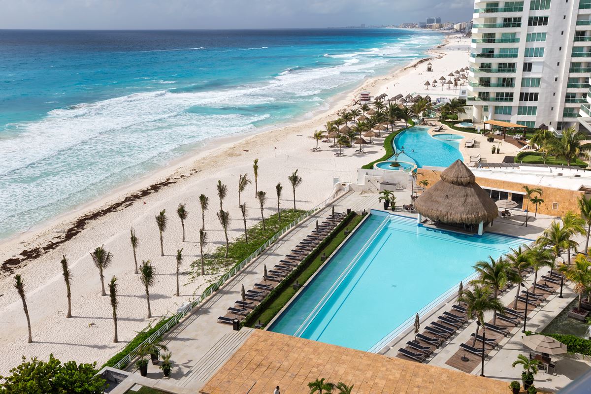Aerial view of a Cancun resort with pool, palapa, sun loungers, and beachfront with palm trees