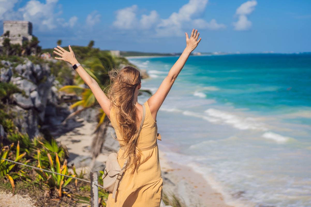 A female traveler with outstretched arms overlooking the beach beneath the Tulum ruins